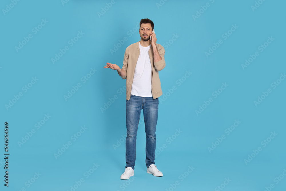 Man talking on phone against light blue background Man talking on phone against light blue background
