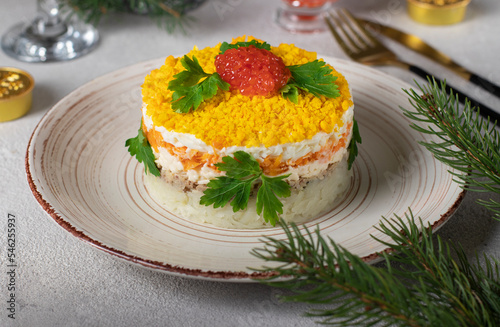 Festive puff salad Mimosa with canned fish, potatoes, cheese, carrots and eggs, garnished with red caviar and parsley leaves