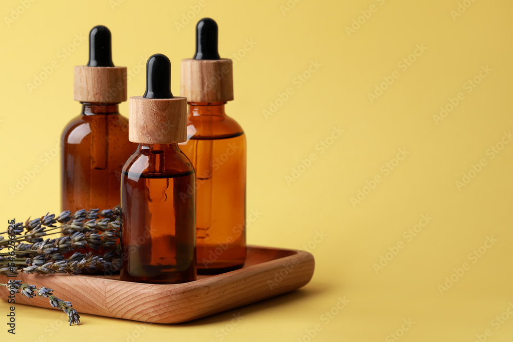 Wooden tray with bottles of face serum and lavender flowers on yellow background, space for text