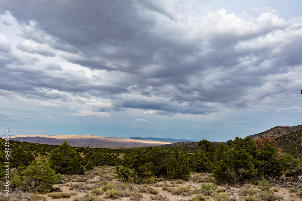 Rain clouds gather on a summer  evening over the Great Basin Desert and Shrublands south of Baker, Nevada near the Utah Border. Rays of sunlight breaking through clouds illuminate a distance mountain.