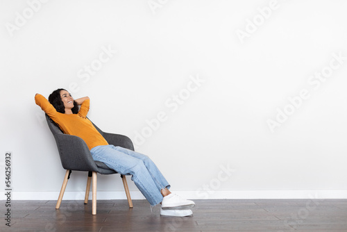 Relaxed young woman reclining in arm chair over white wall
