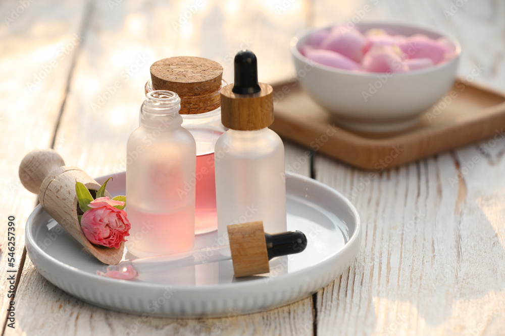 Bottles of rose essential oil and flowers on white wooden table Bottles of rose essential oil and flowers on white wooden table