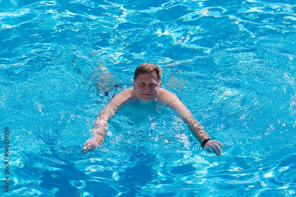 adult European man happily swims in the pool. Luxury holiday concept.