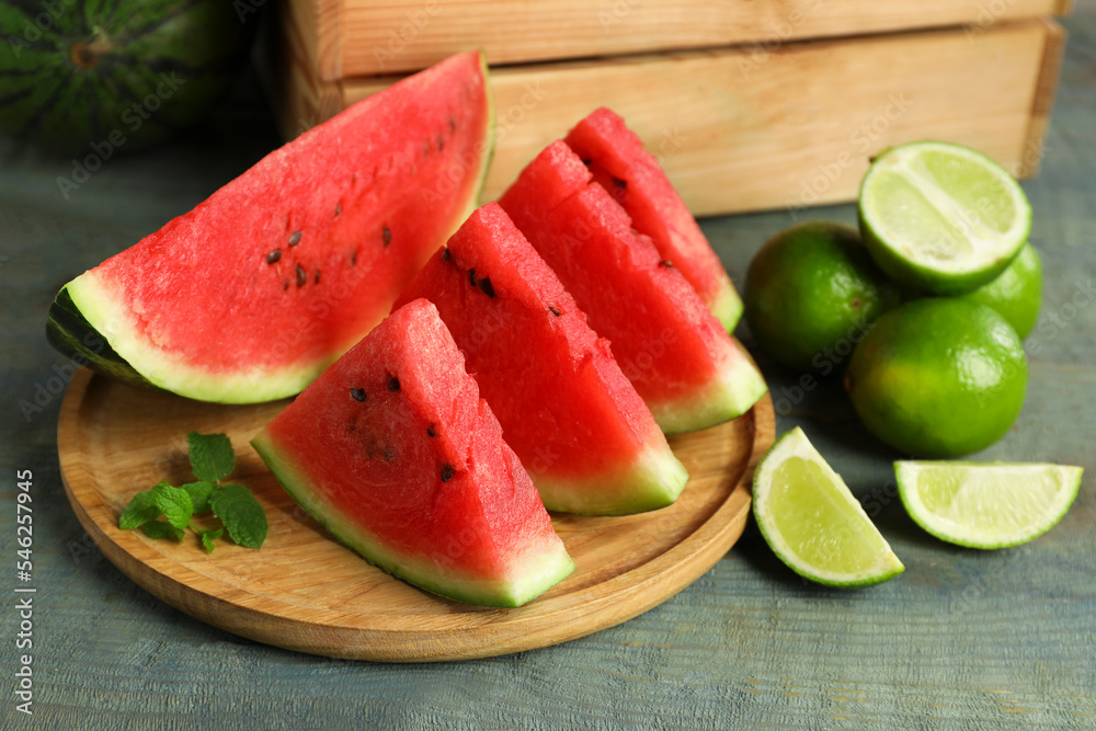 Slices of delicious watermelon, limes and mint on light blue wooden table Slices of delicious watermelon, limes and mint on light blue wooden table