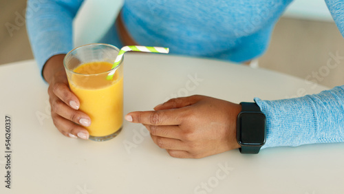 Healthy lifestyle. African american woman in sportswear wearing smart watch and holding glass with orange juice, mockup