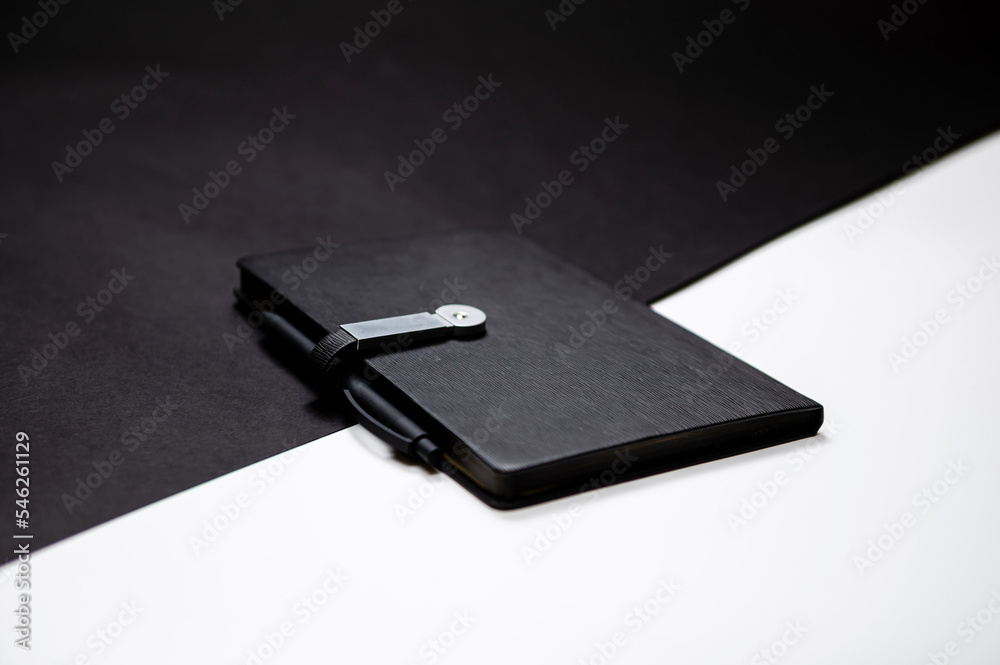 black organizer or notebook with pen on two-color black and white background, mockup, copy space black organizer or notebook with pen on two-color black and white background, mockup, copy space