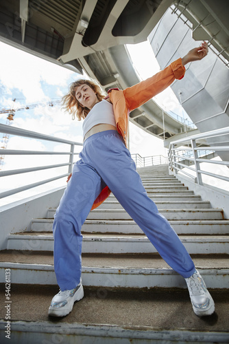 Dynamic full length shot of young woman dancing outdoors in urban area and wearing streetwear photo