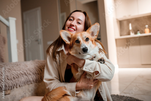Attractive girl hug and play with corgi dog at home. Welsh Corgi Pembroke with his owner woman on the floor at living room © bondvit