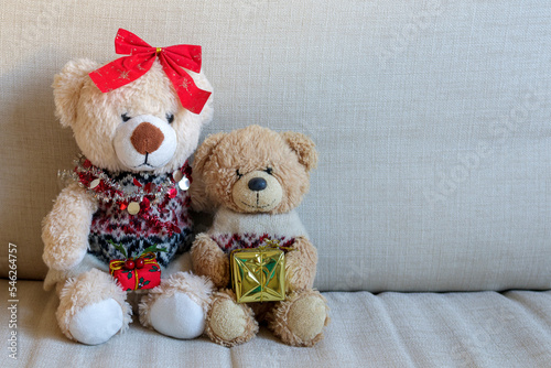 Two small teddy bears sitting on a sofa with Christmas presents
