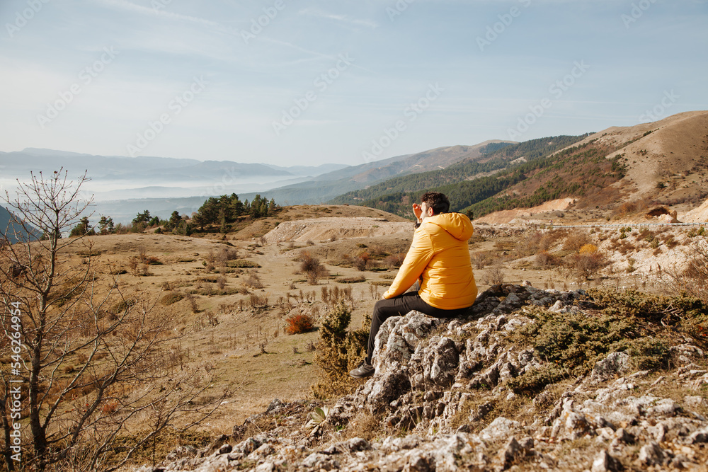 Fototapeta premium Man in a yellow jacket sitting on the rock among the mountains at sunny day in the forest in Turkey Bolu. Hiking concept