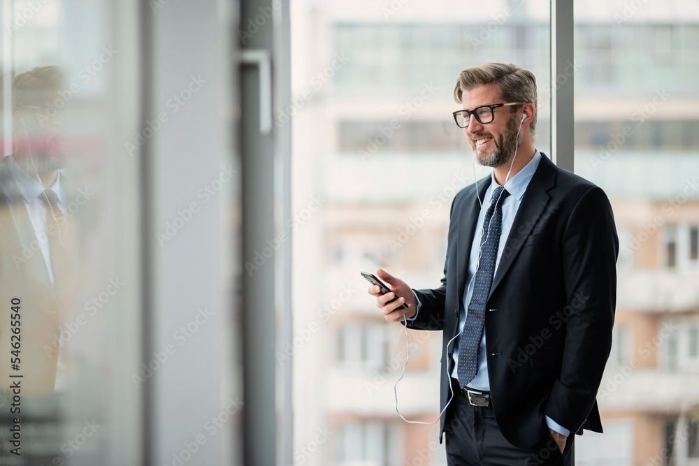 Confident businessman having a phone call and wearing suit and tie while standing at the office Confident businessman having a phone call and wearing suit and tie while standing at the office