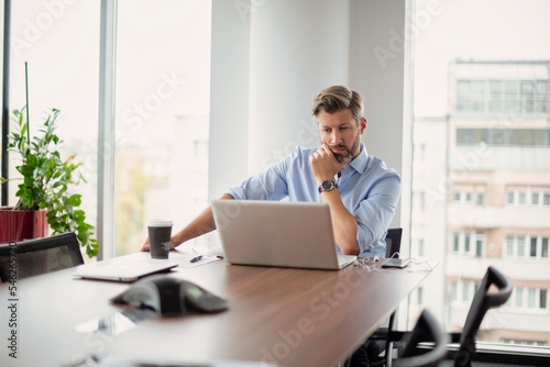  Businessman looking thoughtfully while using laptop at the office