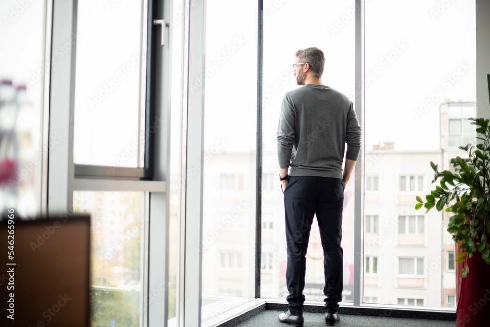 Shot of thinking businesman standing at the office and looking out of city Shot of thinking businesman standing at the office and looking out of city