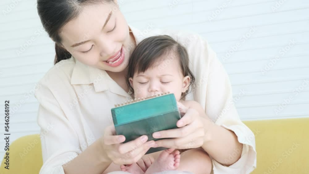 Asian mother playing craft kalimba or wooden mbira instrument with little daughter listen music on sofa. Asian mother playing craft kalimba or wooden mbira instrument with little daughter listen music on sofa.