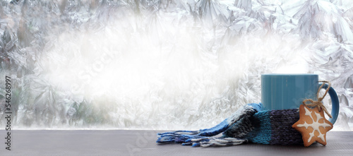 glazed cookies and blue mug wrapped in scarf against frozen window. warming drink on winter morning