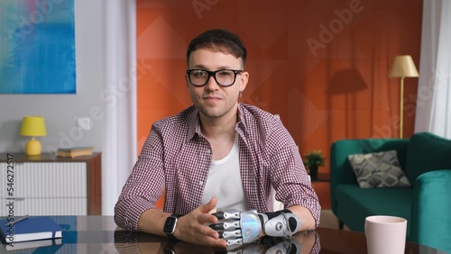 Portrait of young man with hand prosthesis looking at camera and having video call photo