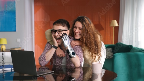 Young woman hug boyfriend with bionic arm working on laptop photo