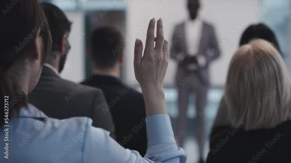 Selective focus rear view of unrecognizable business people raising hands to ask their questions to lecturer
