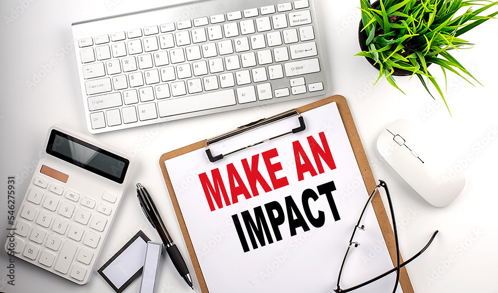 Business concept.Text MAKE AN IMPACT on paper clipboard with,pencil,glasses, keyboard and calculator on white background. Business concept.Text MAKE AN IMPACT on paper clipboard with,pencil,glasses, keyboard and calculator on white background.