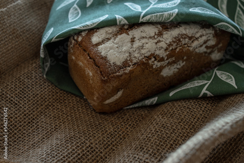 A loaf of bread on a bamboo board, sprinkled with oat flakes, in a burlap bag with garlands