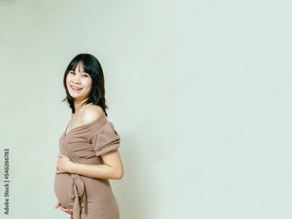 Obraz premium Pregnant happy woman touching her belly with a happy face, Caressing her belly and smiling, Healthy Pregnancy concept on white background, Copy space.