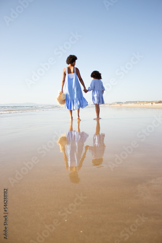 Back view of loving African American family walking on beach. Mother and daughter with dark curly hair spending time together on open air. Leisure, family time, togetherness concept