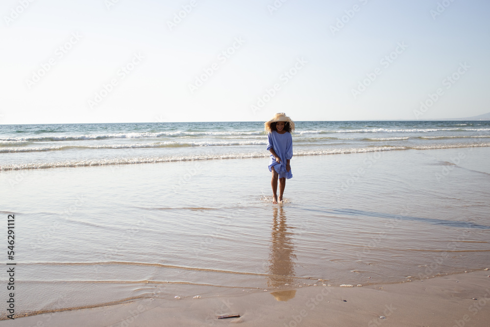Joyful little girl in hat and dress on beach. African American child on beach on summer day. Childhood, portrait, happiness concept Joyful little girl in hat and dress on beach. African American child on beach on summer day. Childhood, portrait, happiness concept