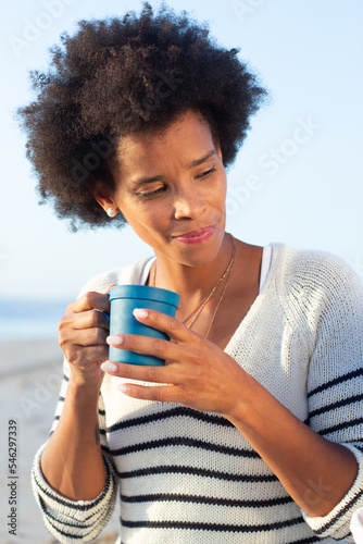 Attractive African American mother on picnic. Woman in casual clothes drinking hot sweet tea from blue mug. Family, relaxation, nature concept