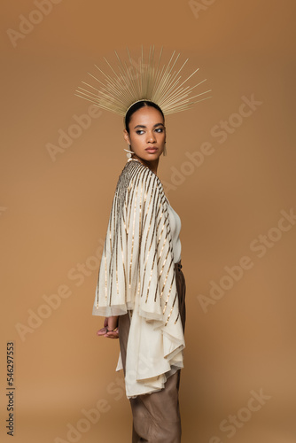 brunette african american woman in earrings and golden crown posing isolated on beige.