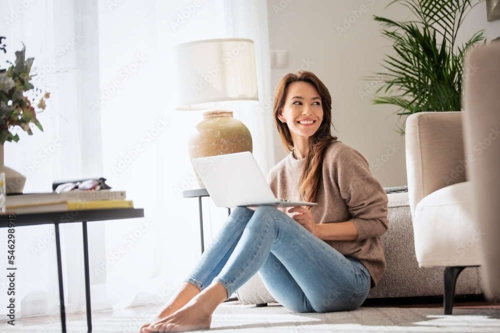 Smiling caucasian woman using laptop at home while sitting on the floor Smiling caucasian woman using laptop at home while sitting on the floor