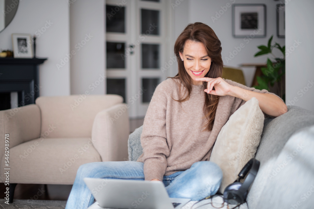 Smiling caucasian woman using laptop at home while sitting ont the sofa Smiling caucasian woman using laptop at home while sitting ont the sofa