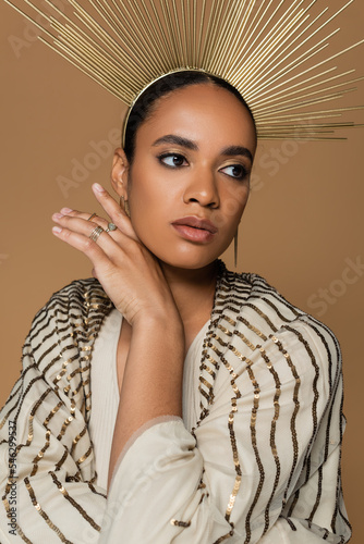 african american young woman in shiny shawl and golden crown posing isolated on beige.