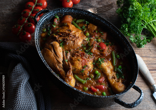 Brown chicken stew with vegetables, potatoes and legumes in a old fashioned pot on wooden table