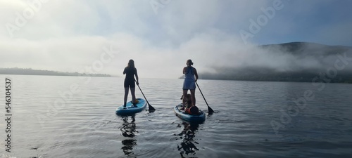 Photography Two young girls on board for Sup surfing raking a wave with  paddle on sunrise