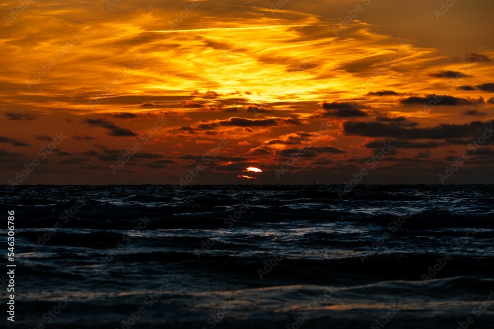 Beautiful view from the beach of the sea with orange cloudy sky at sunset