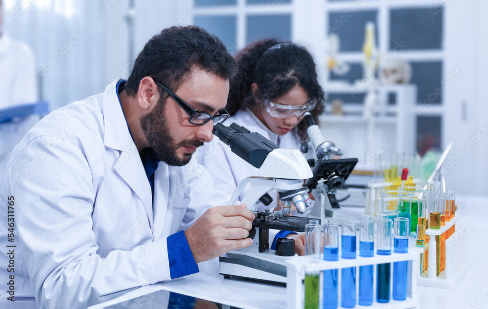 A team of professional male and female scientists working on analyzing samples. Use a microscope and a laboratory lab. A team of professional male and female scientists working on analyzing samples. Use a microscope and a laboratory lab.