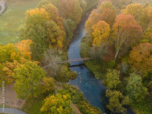 Aerial shot of a river surrounded by trees changing colors for the autumn season