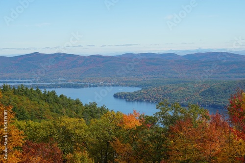 Aerial view of a lake surrounded by dense colorful forests in autumn