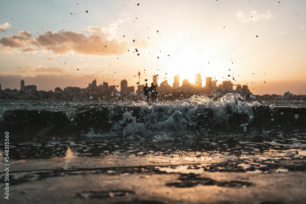 Drops of water from the wave in the sea and buildings on the background during sunset