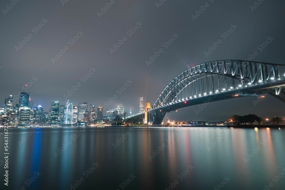 Night shot of Sydney Harbour Bridge and illuminated modern buildings reflected on the water