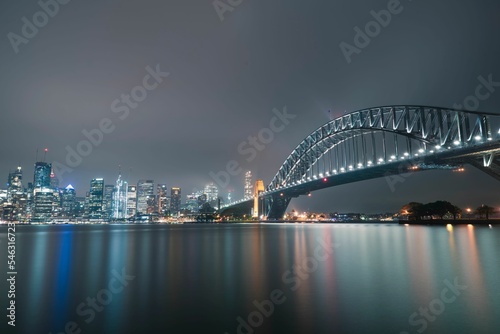 Night shot of Sydney Harbour Bridge and illuminated modern buildings reflected on the water © Daniel Remo/Wirestock Creators