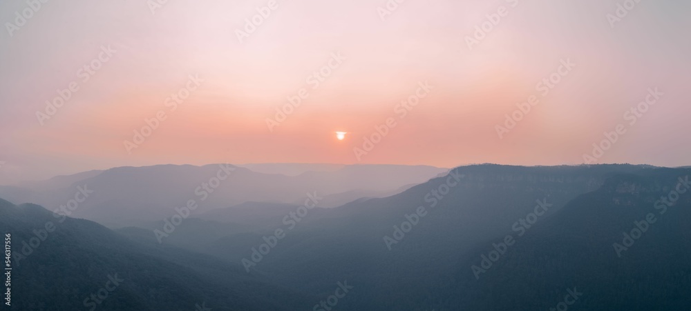 Panoramic shot of the setting sun in the distance and fog covering the hills