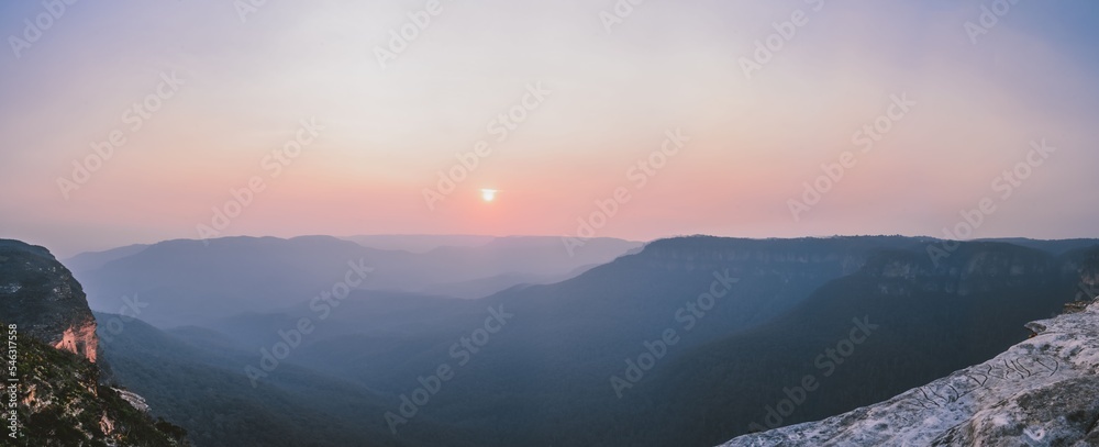 Panoramic shot of the setting sun in the distance and fog covering the mountains