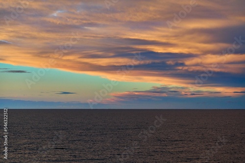 Scenic shot of a calm seascape during an orange sunset with clouds in the sky © Chris West/Wirestock Creators