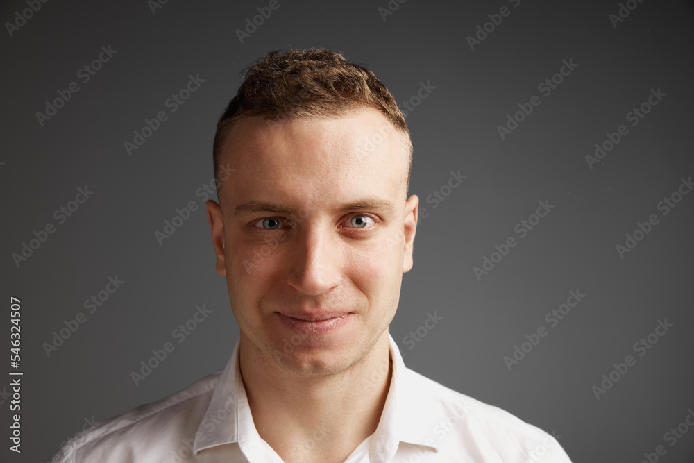 Close-up portrait of young businessman attentively looking at camera, posing isolated over grey studio background