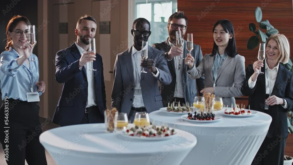 Group portrait of six ethnically diverse business people standing in front of buffet tables served with drinks and snacks raising glasses with champagne smiling at camera Group portrait of six ethnically diverse business people standing in front of buffet tables served with drinks and snacks raising glasses with champagne smiling at camera