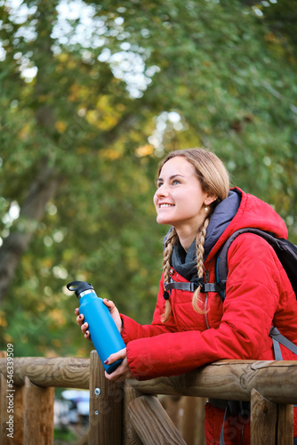 Young female hiker holding water bottle contemplating views in the forest.