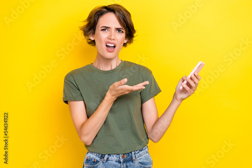 Photo of upset unsatisfied woman bob hairdo dressed khaki t-shirt palm directing at smartphone isolated on yellow color background