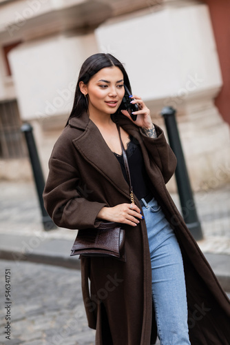 positive and stylish brunette woman talking on smartphone on street in prague. photo