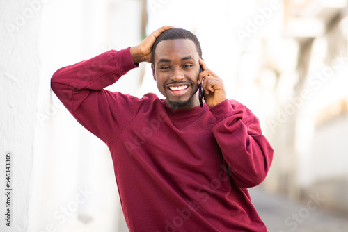 Smiling black man leaning to wall and talking on cellphone outdoors